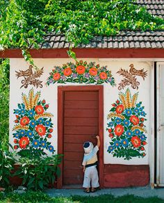 a young boy standing in front of a painted wall with flowers and leaves on it