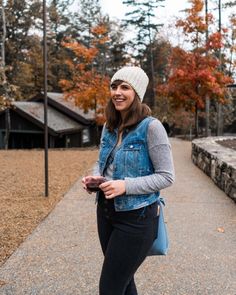 a woman is standing on the sidewalk in front of some trees and holding a cell phone