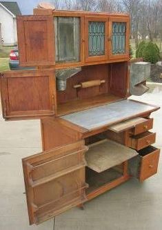 an old fashioned wooden desk with drawers and cupboards on the top shelf, in front of a house