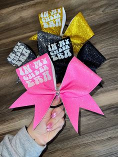 A standard sized hair bow made with 3 inch grosgrain ribbon and a glitter heat transfer vinyl overlay. The vinyl base comes in different colors, and has a white HTV decal on it with the words "In My Cheer Era". The bow has a rhinestone center and is on a ponytail holder to be worn in the hair. Cheer Bows Ideas, Photo Coasters Diy, Cheer Competition Bows, Dance Team Bows, Cheer Bow Holder, Competition Cheer Bows Rhinestones, Pink Cheer Bows, Custom Cheer Bows, Softball Bows