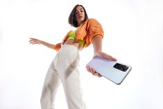 a woman in an orange top is holding a white and black electronic device with her right hand