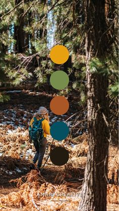 a woman hiking through the woods with colorful circles hanging from trees in front of her