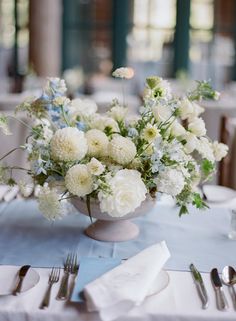 a vase filled with white flowers sitting on top of a table next to silverware