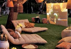 an outdoor movie is set up in the grass with lights strung over it and pillows on the ground