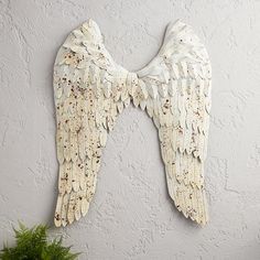 two white angel wings hanging on the wall next to a potted plant and vase