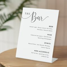 a white menu card sitting on top of a wooden table next to a potted plant