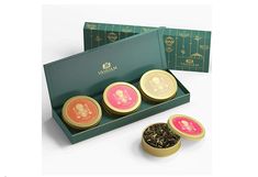 three tea tins in a green box with gold trimming and pink labels on them