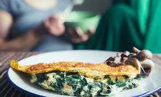 an omelet with spinach and mushrooms on a plate next to a woman