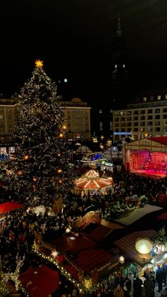 a large christmas tree is lit up in the middle of a crowded city at night