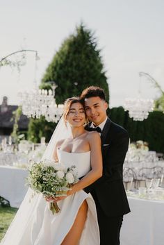 a bride and groom pose for a photo in front of an outdoor table with chandeliers