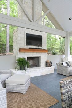 an outdoor living area with couches, chairs and a television on the fireplace in the center