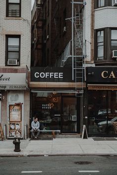 a man sitting on the sidewalk in front of a coffee shop