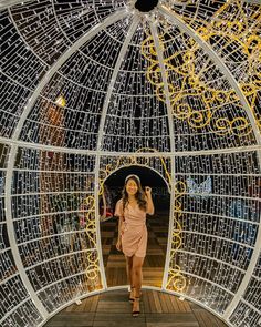 a woman in a pink dress is walking through a glass structure with lights on it