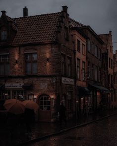 people are walking down the street with umbrellas on a rainy night in an old european town