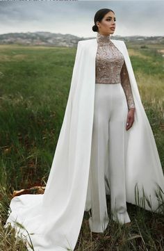 a woman standing next to a horse wearing a white gown and cape with long sleeves