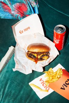 a hamburger and french fries are sitting on a green couch next to a can of soda