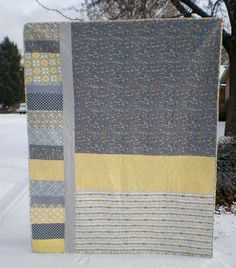 a quilted blanket sitting on top of snow covered ground next to a tree in the background