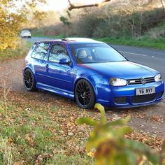 a blue vw golf wagon parked on the side of a road next to trees