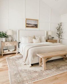 a bedroom with white walls and wood flooring has a bed, two nightstands, and a bench