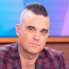 a man with short hair wearing a red and black checkered shirt sitting in front of a tv