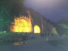 people are standing in front of an old building with lights on it at night time