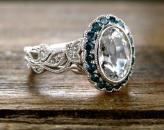 an oval shaped ring with blue and white stones on the side, sitting on top of a wooden table