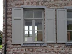 two windows with white shutters on the side of a brick building