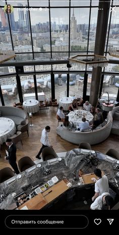 people are sitting at tables in the middle of a room with high ceilings and floor to ceiling windows