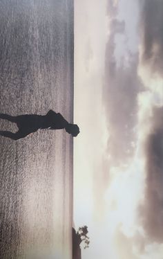 a person standing on the edge of a body of water with clouds in the background