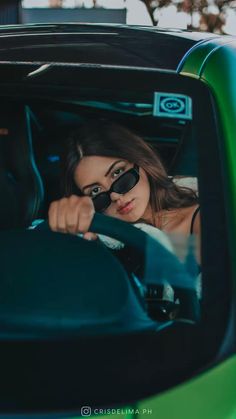 a woman wearing sunglasses sitting in the driver's seat of a green car