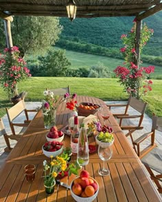 a wooden table topped with bowls of fruit and vegetables on top of a lush green field