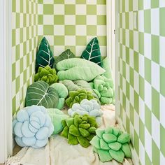 a room with green and white checkered walls, pillows and plants on the floor