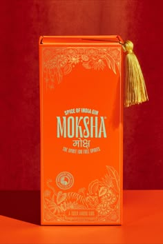 an orange box with the words moksha on it and a tassel hanging from it