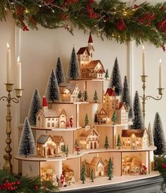 a christmas tree made out of wooden houses and trees with lit candles on the mantle