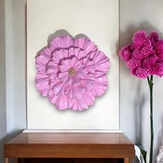 a pink flower sitting on top of a wooden table next to a vase filled with flowers