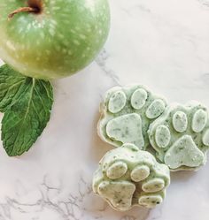 an apple and two cookies on a marble surface next to each other with green leaves