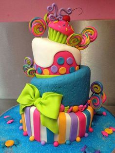 a multi - tiered cake decorated with colorful icing and bows on a blue plate