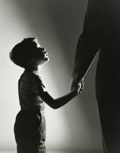 a black and white photo of a young boy holding the hand of an adult