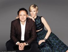 a man and woman sitting next to each other on a gray background posing for the camera