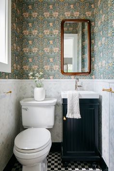 a white toilet sitting next to a sink in a bathroom under a mirror on top of a wall