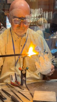 a man in yellow shirt and glasses working on a piece of metal with flames coming out of it