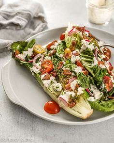 lettuce and tomato salad with dressing on a plate next to a glass of water