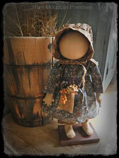 a doll is standing next to a wooden barrel and wearing a hat with flowers on it