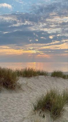 the sun is setting over the ocean and sand dunes