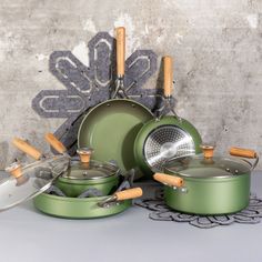 an assortment of green pots and pans with wooden handles on a doily in front of a concrete wall