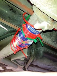 a red bucket filled with paint sitting on top of a metal pipe under a car