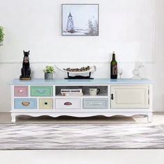 a white entertainment center with colorful drawers and vases on the top, in a living room