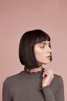 a woman with short black hair wearing a turtle neck sweater and looking off to the side