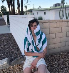 a woman sitting on the side of a wall with her hands under her chin and wearing a towel around her neck