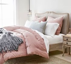 a bed with pink comforter and pillows in a bedroom next to a window on a rug